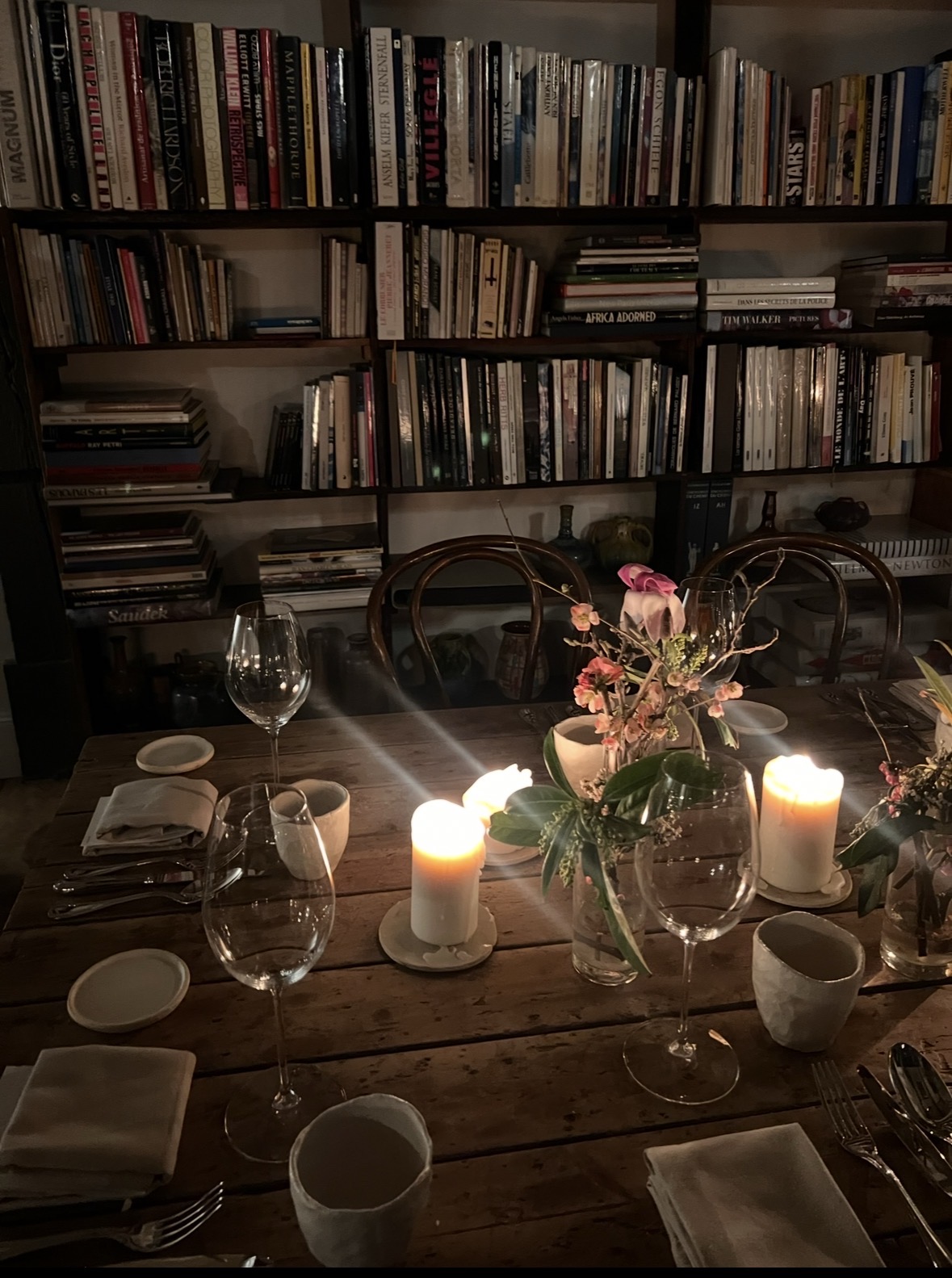 A candlelit table set for dinner among books and flowers